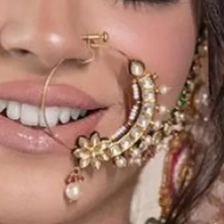 A close-up of a model wearing a delicate floral-motif nath. This beautiful nose ring is available for rent.