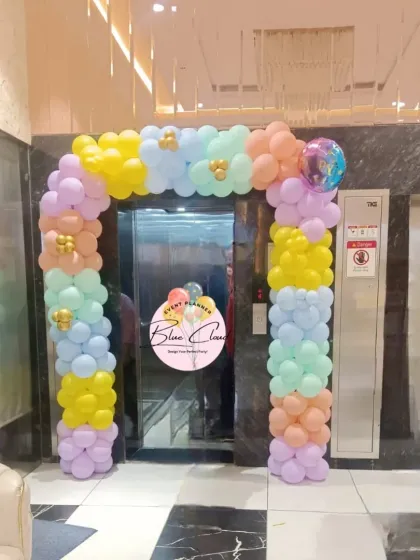 A pastel-colored balloon arch framing an elevator entrance, welcoming guests to the party.