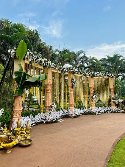A wide view of a traditional South Indian style decor setup, with carved pillars draped in flower garlands and large banana leaf arrangements.