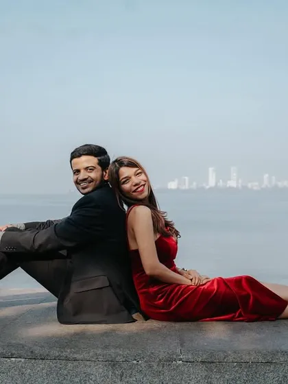 A relaxed and happy pose, sitting back-to-back against the sea wall, showcasing the couple's comfortable and playful relationship.