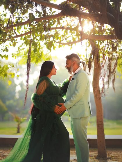 A romantic outdoor portrait of a couple, with the mother-to-be in a stunning green gown. The golden hour light filters through the trees, creating a magical atmosphere.