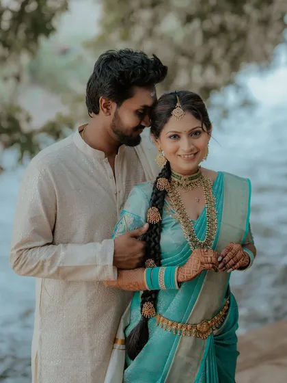 A sweet couple portrait by the water. The bride's vibrant blue saree and the groom's simple white dhoti create a beautiful contrast.