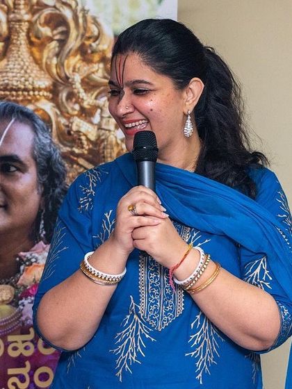 A speaker sharing insights during a Bhakti Marga event, with a backdrop of the spiritual guru Paramahamsa Vishwananda.