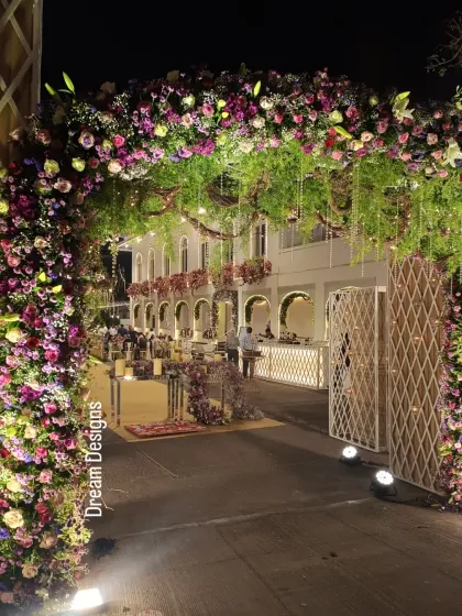 A closer look at the magnificent floral entrance arch at night. The dense arrangement of purple and pink flowers, combined with cascading greenery, creates a rich and welcoming passage for guests.