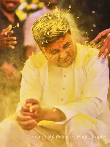 A candid action shot of the groom during the Haldi ceremony, wincing with a smile as he's covered in turmeric paste and petals. These are the fun, real moments you'll want to remember.