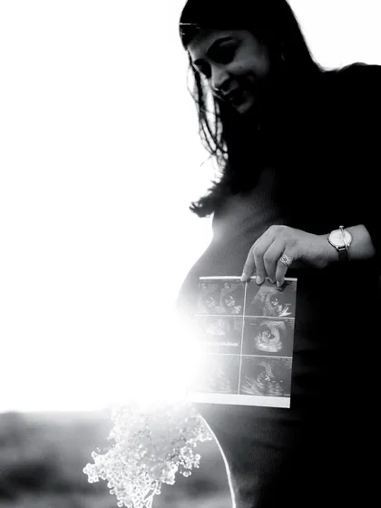A high-contrast black and white shot where the sun flares behind the mom-to-be, creating a halo effect as she looks at her sonogram. It's a very artistic detail shot.
