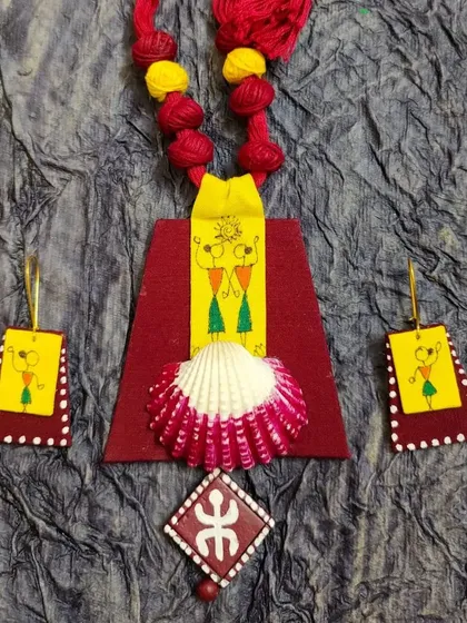 A fusion of styles, this piece combines hand-painted Warli figures with a painted seashell centerpiece. The vibrant yellow and red fabrics create a cheerful backdrop for the tribal motifs and natural elements. The design is a playful mix of different textures and inspirations.