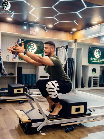 This squat variation on the reformer box with a magic circle challenges lower body strength and core stability simultaneously. The focus is on maintaining balance and control throughout the movement.