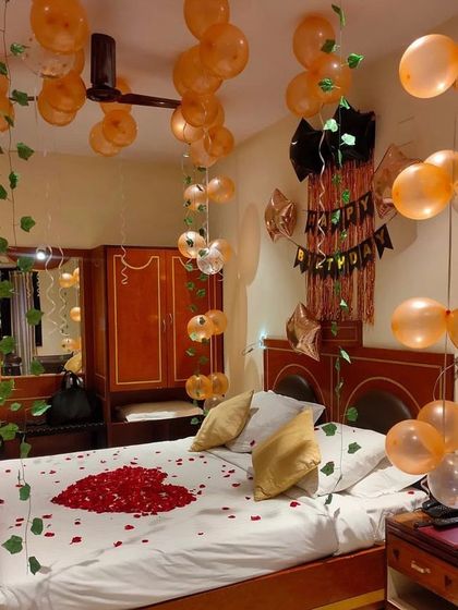 A nature-inspired romantic birthday setup, combining orange balloons with green ivy vines and a heart of rose petals on the bed.