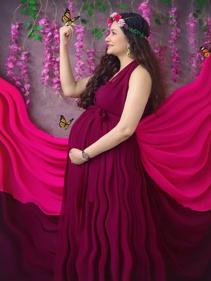 Feeling like a goddess in this whimsical studio setup. The flowing magenta gown, flower crown, and magical butterflies create a truly enchanting maternity portrait.