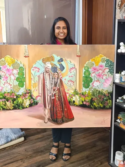 Holding the large, completed canvas of the Pichwai-themed wedding painting.
