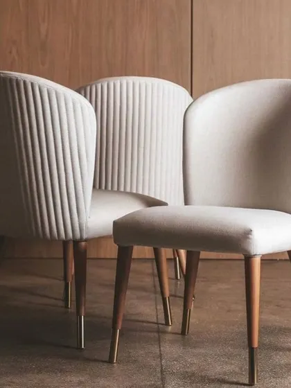 These elegant dining chairs feature two different back styles: one with vertical pleating and one with a smooth curve. The tapered wooden legs with brass tips add a mid-century modern touch.