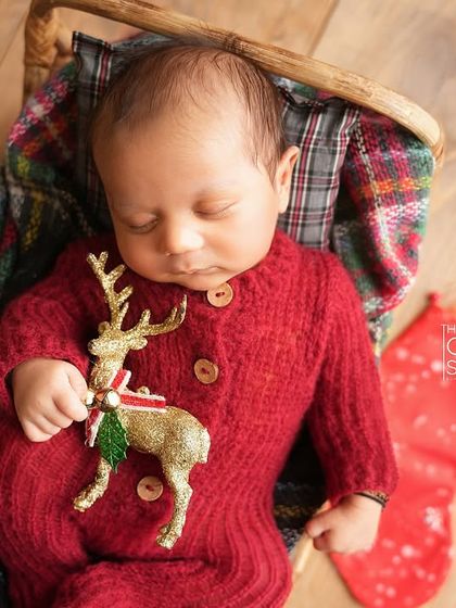 An overhead shot of a newborn in a red knit outfit, holding a tiny reindeer prop. This highlights the festive details and the baby's serene expression.