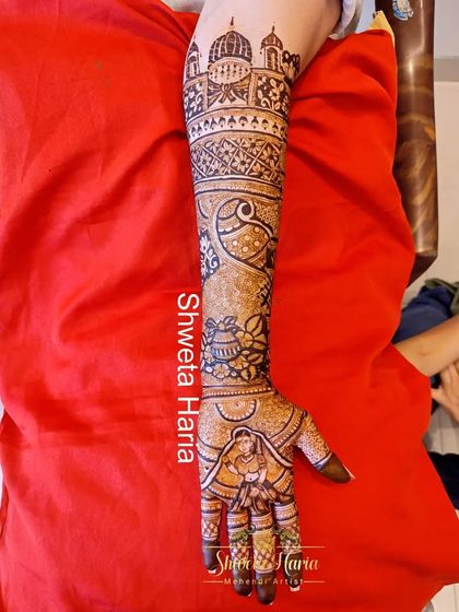 A side view of a full bridal arm, this design features a bride portrait on the palm, peacock motifs, and architectural details reaching up to the elbow.