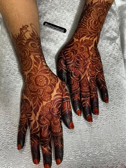 A gorgeous, fully developed henna stain. The design combines floral elements with traditional patterns, and the initials 'MP' are subtly included at the wrist.