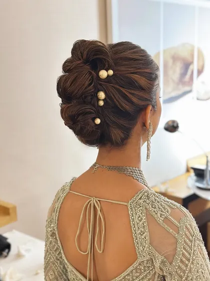 A closer look at a "perfectly undone" textured updo. The interwoven sections create volume and dimension, while the scattered pearl pins add a touch of modern elegance, making it a popular choice for reception looks.