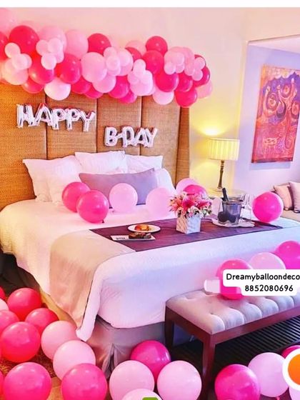 A pink-themed birthday surprise in a hotel room. The decoration includes 'HAPPY B-DAY' foil balloons over the bed, with pink balloons scattered on the floor and bed for a fun, celebratory feel.