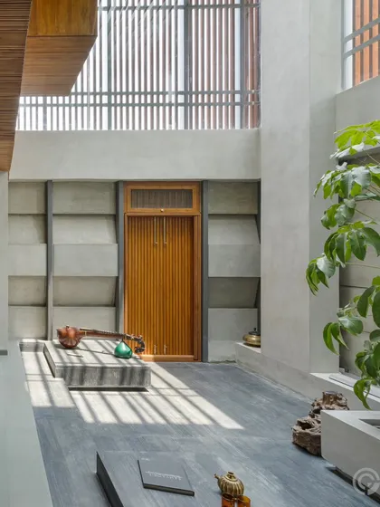 An internal courtyard, or 'angan', brings natural light deep into the home through a double-height volume. The textured, precast concrete blocks on the wall create a beautiful pattern as sunlight filters through the slatted screen above, connecting the interior with the rhythm of the day.