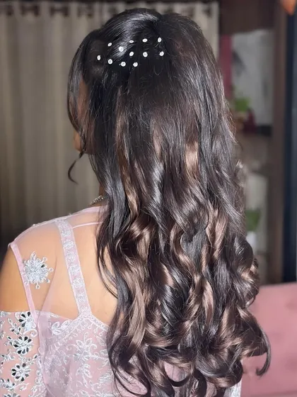 A detailed shot of a beautiful sangeet hairstyle. Soft curls are gathered into a half-up style, adorned with delicate pearl pins for a touch of elegance.