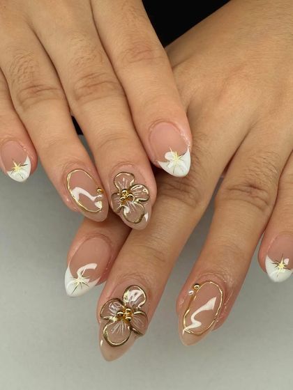 A beautiful combination of French tips and 3D art. This set features sculpted gold flowers and gold chrome outlines on a nude base.