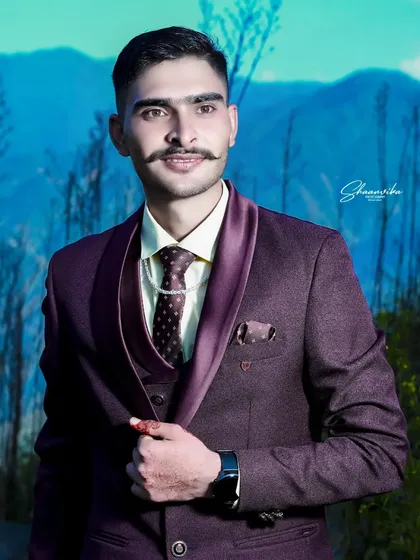 A sharp and stylish groom portrait taken outdoors. The crisp mountain air and bright blue sky provide a stunning natural backdrop, making the groom's formal suit stand out. This is a great option for a wedding album or individual portfolio.