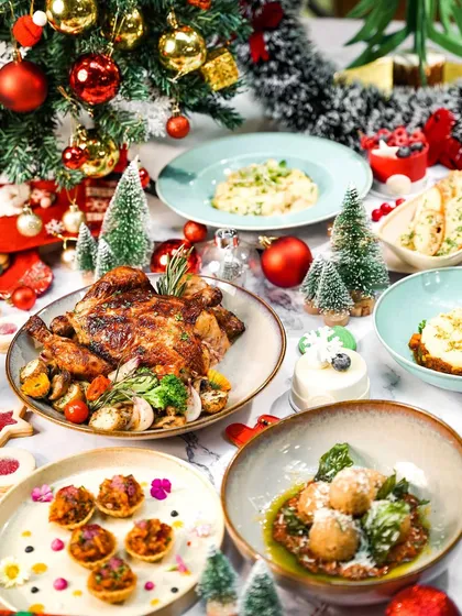 A side view of a festive Christmas brunch table, showing the depth and variety of the spread. The decorated tree in the background adds to the merry atmosphere.