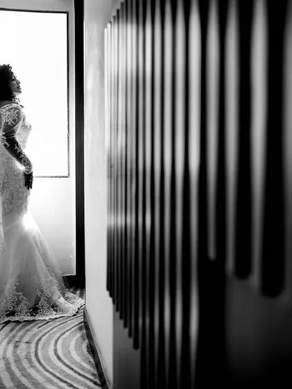 A dramatic bridal silhouette shot against a bright window. This black and white image uses strong contrast and composition to create a powerful and elegant portrait, capturing a quiet moment of reflection for the bride on her wedding day.