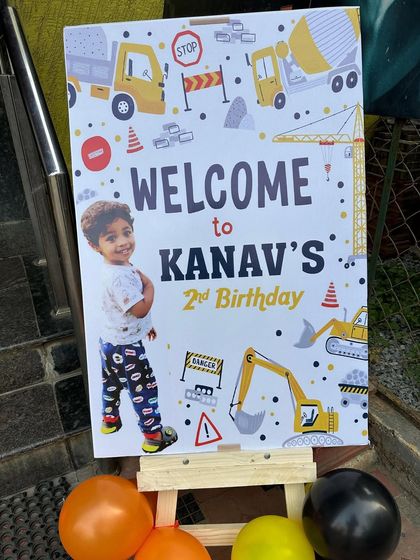 A personalized welcome sign for a construction-themed second birthday. It features the birthday boy's photo along with fun graphics of trucks and excavators.