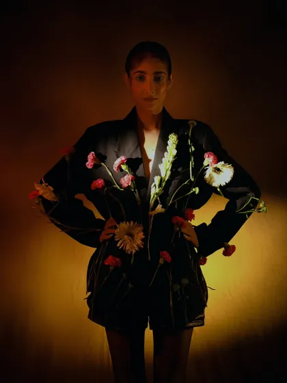 A dramatic, low-key version of the floral portrait. The model is silhouetted against a warm glow, creating a mysterious and powerful image.