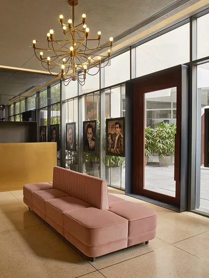 The theater lobby is adorned with framed portraits of film icons along the glass façade, with a long pink sofa providing a pop of color.