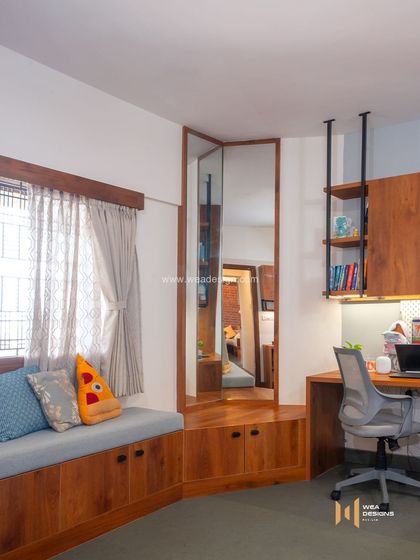 A clever use of space in a bedroom, combining a window seat with a compact study desk and a corner dressing unit with a full-length mirror.