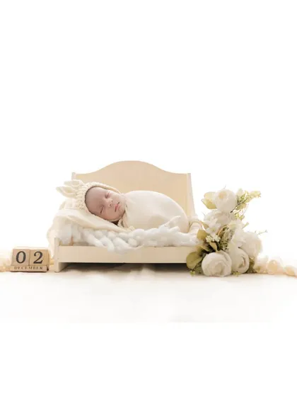 A sleeping newborn lies on a miniature bed, with wooden blocks indicating the date. This is a beautiful way to commemorate the baby's birth date while creating a delicate and artistic portrait.
