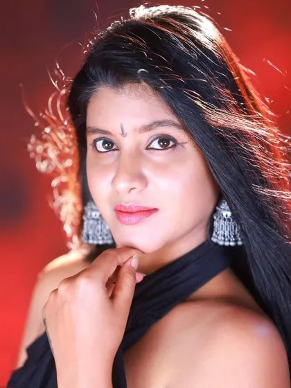 A beautiful close-up portrait against a dramatic red and black studio background. The focus is on the model's expression and the silver 'jhumka' earrings.