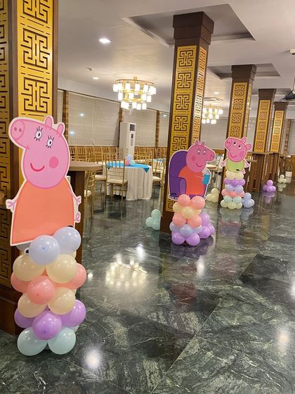 A fun Peppa Pig themed party setup in a banquet hall. The decor includes character cutouts on balloon pillars, creating a playful atmosphere.