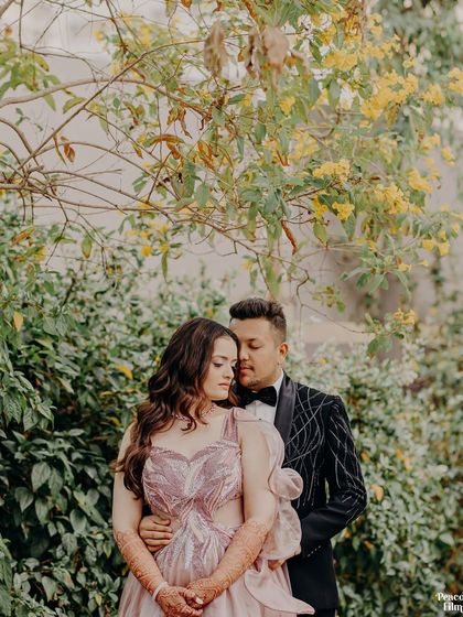 A romantic portrait of the couple surrounded by nature. The groom embraces the bride from behind, both lost in a quiet, happy moment.
