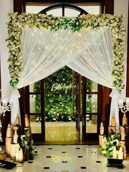 An elegant and welcoming entrance designed for a pre-wedding function at home. White floral arrangements, draped fabric, and warm candlelight transform the doorway into a grand entryway.