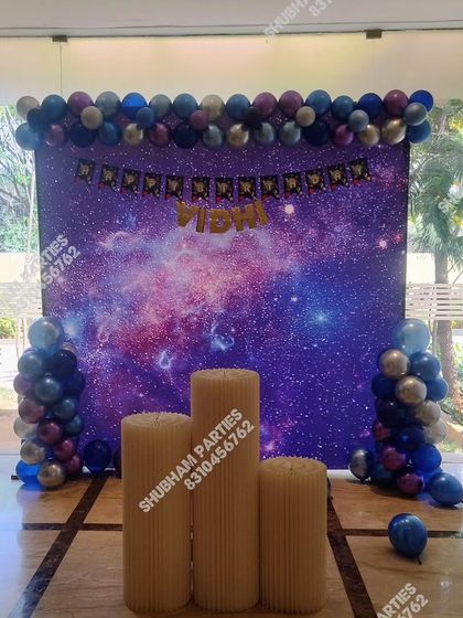 A cool galaxy themed birthday party with a nebula print backdrop and blue and silver balloons.