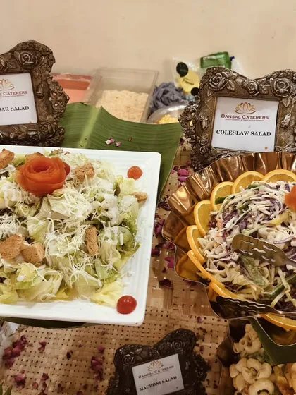 A side-by-side display of my creamy Caesar salad with croutons and a colorful coleslaw salad garnished with orange slices.