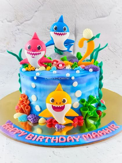 Baby Shark doo doo doo. This vibrant underwater cake features the whole Baby Shark family, handcrafted from fondant. The design uses an airbrushing technique on buttercream to create the blue ocean effect.