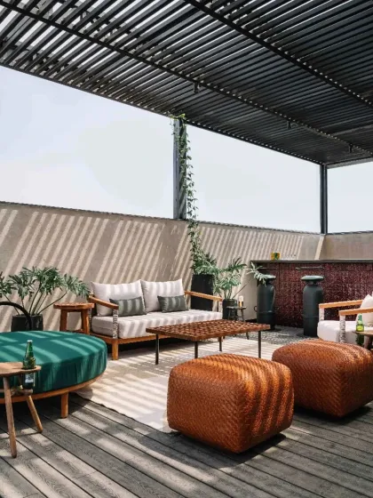 The rooftop lounge of Project 1374, sheltered by a metal pergola that casts shifting patterns of light and shadow. The space is furnished with a mix of modern and handcrafted pieces, creating a relaxed yet sophisticated entertainment zone.