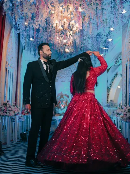 A perfect reception moment. The groom twirls his bride, showing off her sparkling red lehenga under the grand chandeliers.