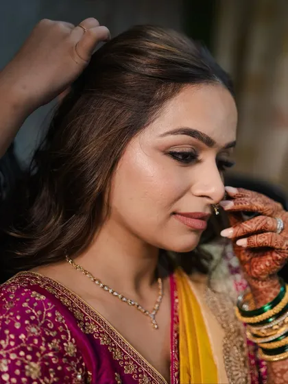 A quiet moment during hair styling. The makeup is already done, showcasing a flawless base and a soft, defined eye, ready for the final hairstyle.