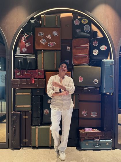 Posing against a creative wall of vintage luggage. As a destination wedding DJ, I'm always on the move, collecting memories and experiences along the way.