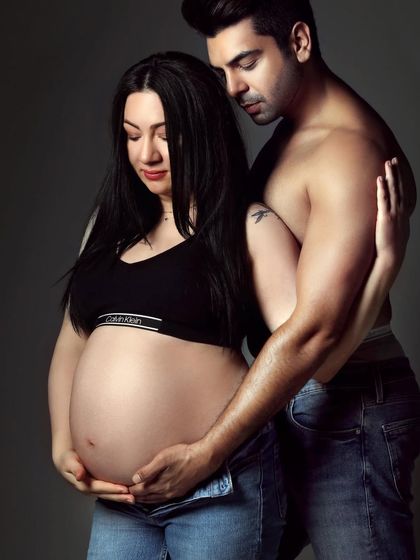 A modern and intimate couple's maternity portrait. This style, with a simple grey backdrop and casual outfits, focuses on the raw connection and anticipation between the expecting parents.