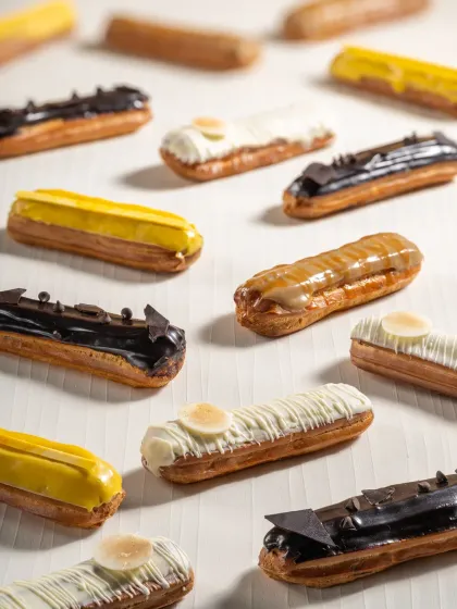 A pattern of assorted eclairs with different toppings like chocolate, white chocolate, and caramel, creating a visually interesting flat lay.