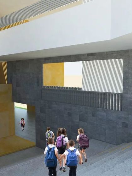 An interior view of a common area within the school, designed with multi-level pathways and ramps to encourage student interaction. The contrast between the raw concrete and warm yellow walls creates a vibrant and dynamic atmosphere.