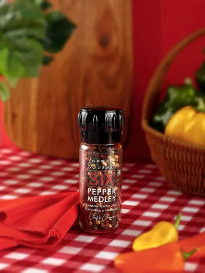 A rustic, warm lifestyle scene for Sprig's Pepper Medley. The checkered tablecloth and fresh vegetables create a cozy, farm-to-table feel that highlights the product's quality ingredients.