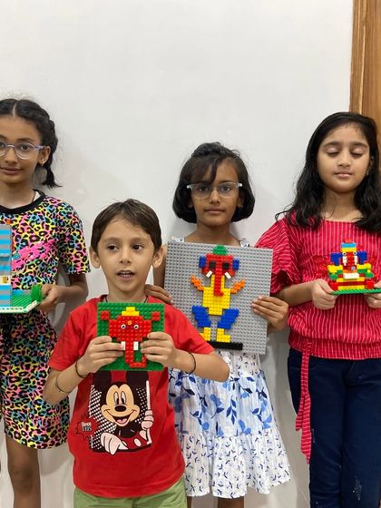 A group of four children proudly present their finished LEGO creations from our Ganpati workshop. Each child has built a different model, from a mosaic-style Ganesha to smaller, colorful idols, showing the variety of projects we offer.