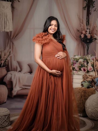 Wrapped in a warm, earthy hue. This rust-colored tulle gown features a lovely one-shoulder floral detail and a flowing skirt, creating a beautiful look in this boho-chic studio setup.