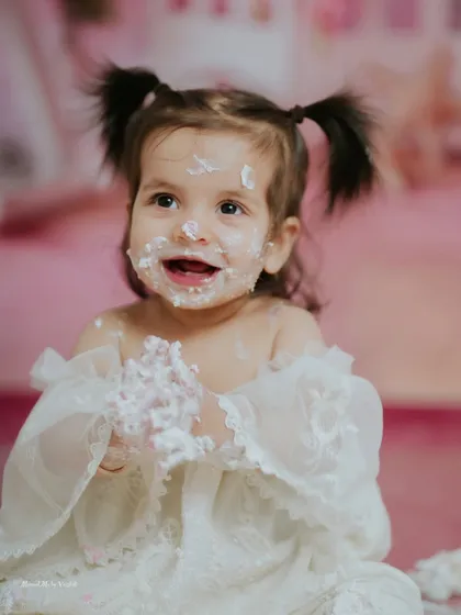 The smile says it all. This little girl, with her adorable pigtails and lacy white dress, is loving every second of her pink themed cake smash.